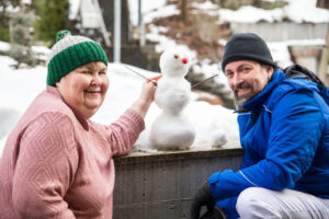 one women and one man outside in the slow. They are posing with a little snowman.