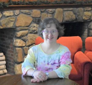 A women sitting in a orange chair with a tie die shirt one.