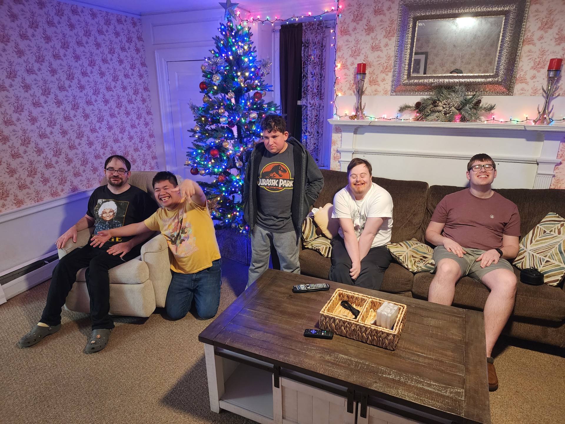 Five young men pose in their living room in front of a Christmas tree, smiling.